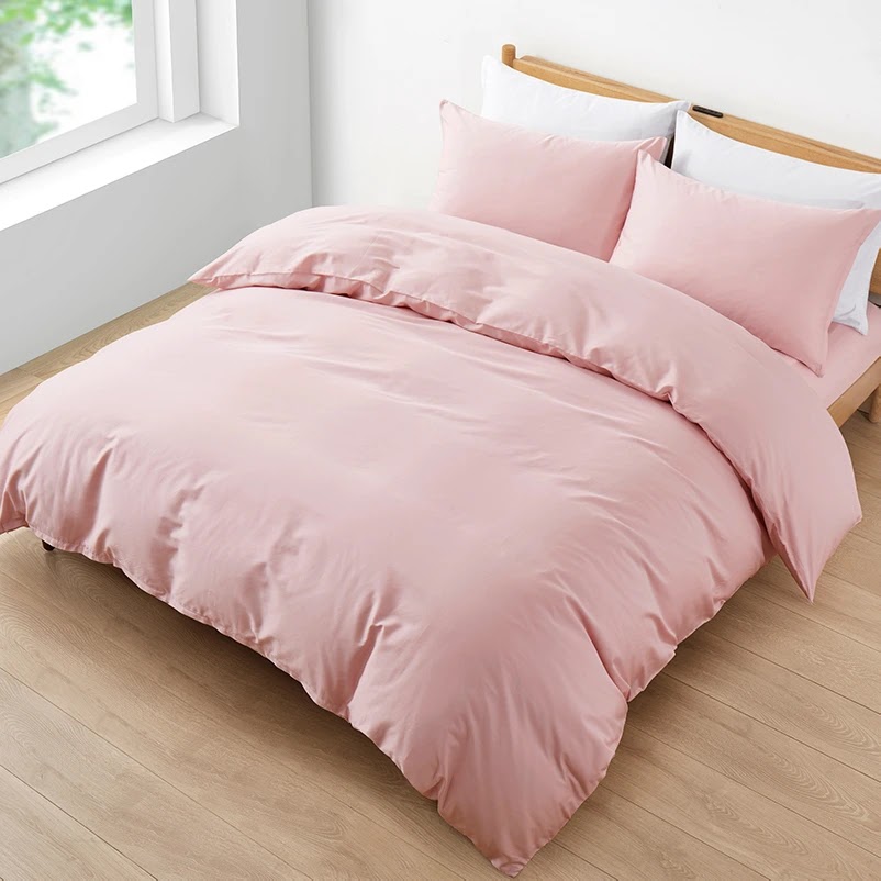 Pink anti-allergy duvet cover and pillows on a wooden bed frame beside a sunlit window