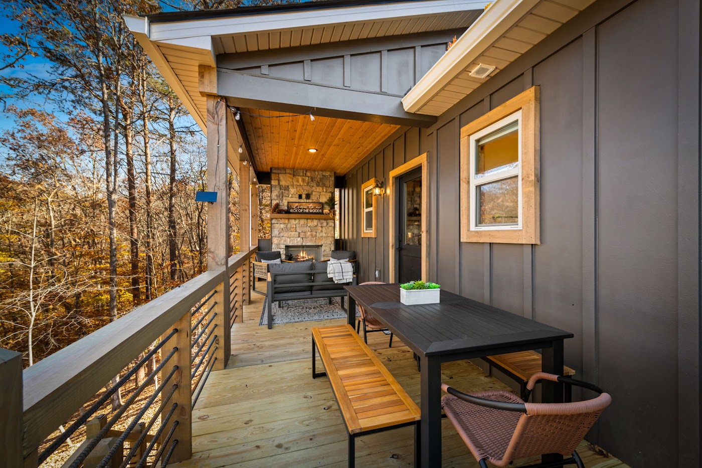 Covered back deck with stone outdoor fireplace and dining table surrounded by fall trees at Orchard & Vine Mountain Haus, Ellijay, Georgia