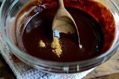 Sau đó nhắc tô chocolate xuống, cho 1/4 muỗng cà phê bột quế, 1/2 muỗng cà phê tinh chất vani, 1/2 muỗng cà phê dầu dừa. Trộn đều cho tất cả hòa quyện vào nhau. Chế sốt chocolate ra tô nhỏ khác là chúng ta hoàn thành rồi đó.
