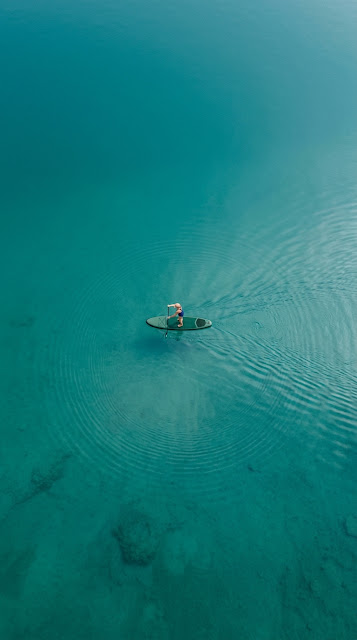 Aerial View of Lone Paddleboarder on Turquoise Lake - Free mobile Wallpaper