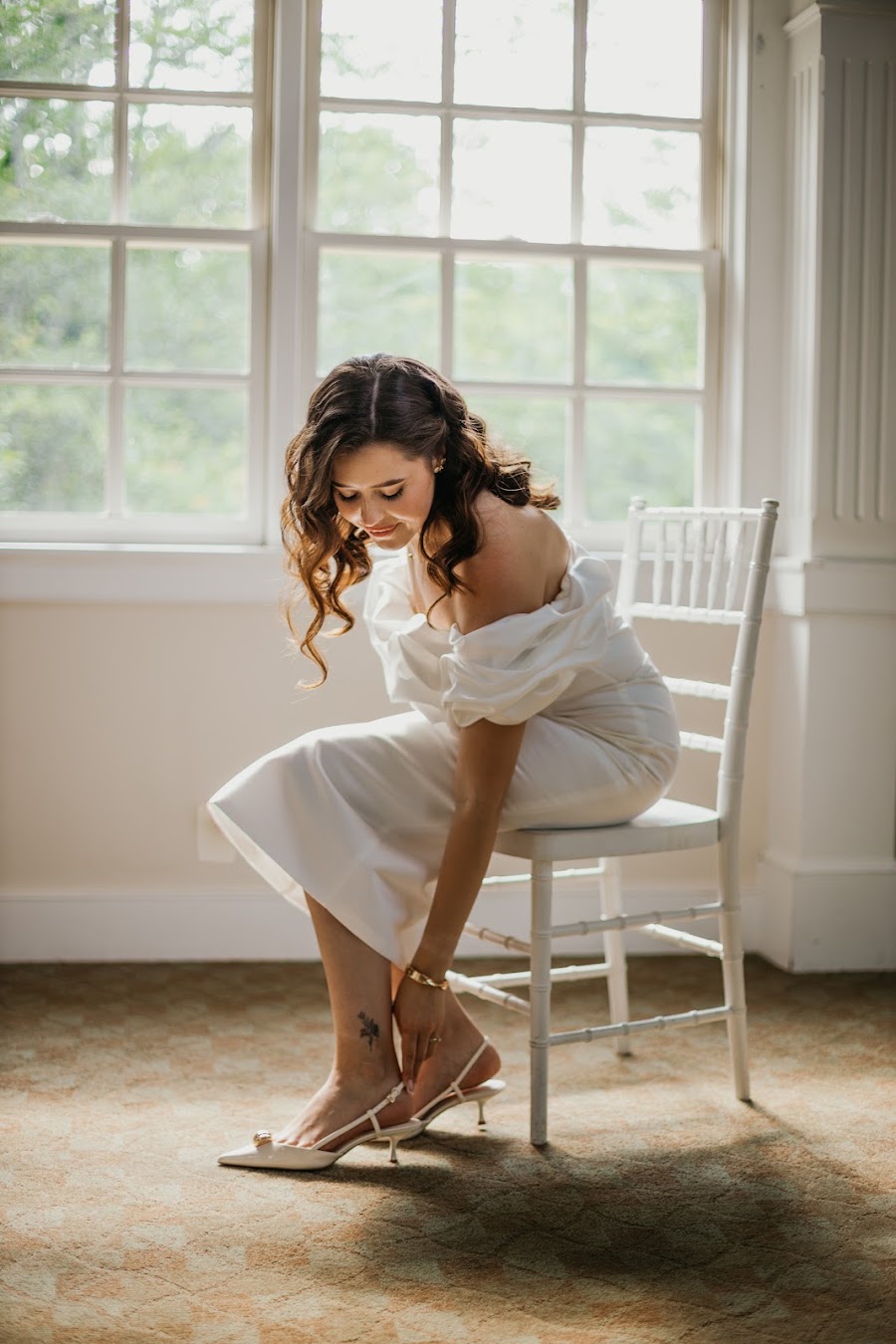 Bride fastening her shoe by the window — candid bridal portrait