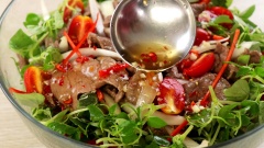 Cho 300gr rau càng cua, 100gr cà chua bi bổ đôi vào tô trộn, trút nhanh cả chảo thịt bò vào tô, thêm 20gr ớt sừng thái chỉ. Đổ nước mắm trộn gỏi vào trộn nhanh tay. Hơi nóng từ thịt sẽ làm rau dậy mùi thơm và tái vừa đủ.
