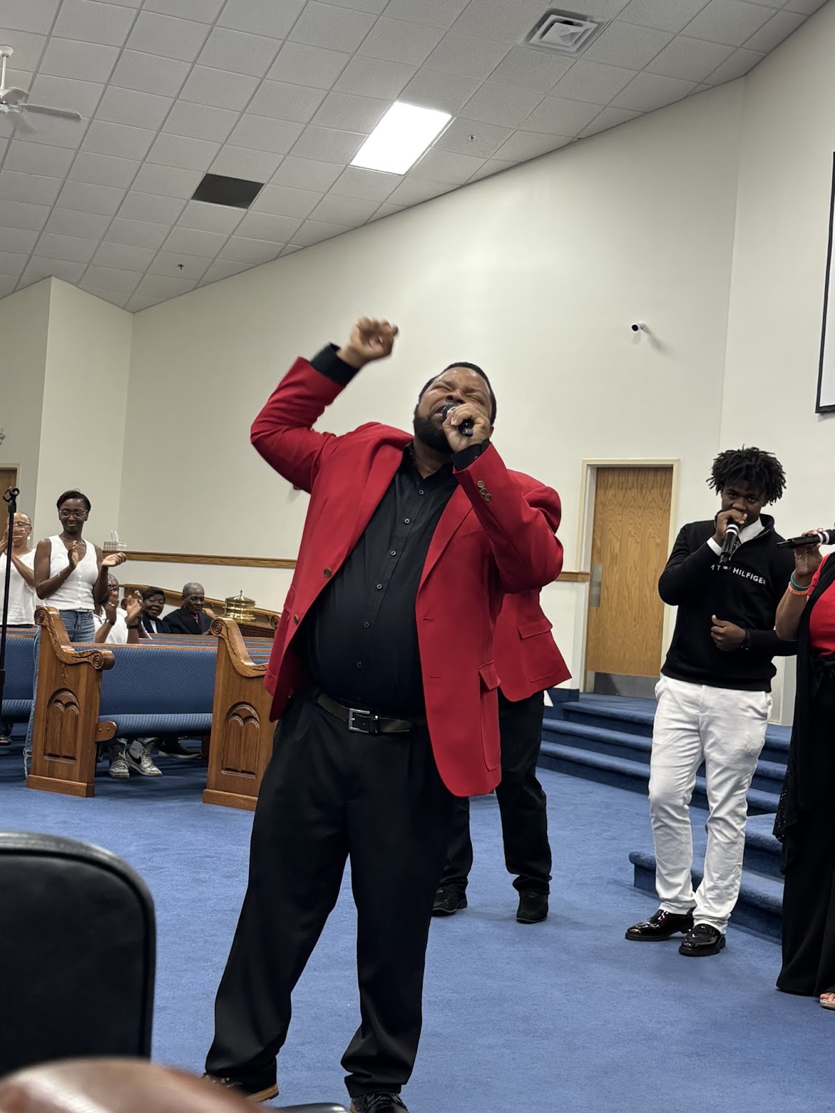 Praise leader in red blazer with raised fist in worship at Homecoming 2026
