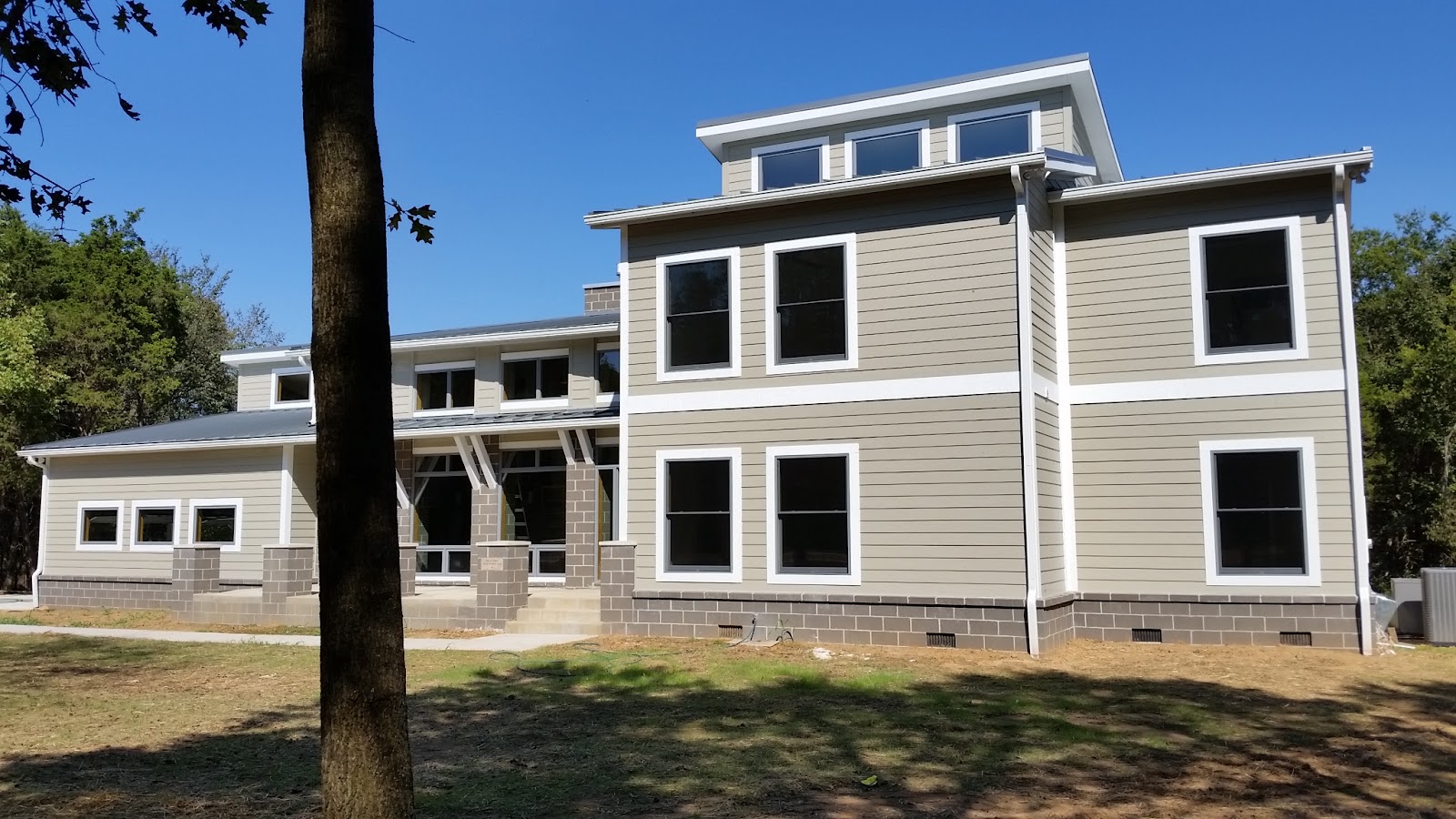 Exterior of a multi-story home with tan siding, white trim, and dark-framed windows above a grey masonry block foundation.