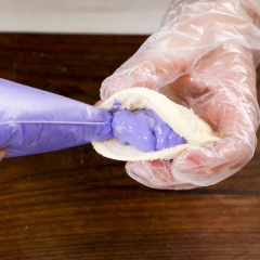Dùng kéo cắt rìa của bánh sandwich, cán dẹt bánh rồi dùng khuôn tạo hình tròn (hoặc hình khác tùy theo sở thích của bạn), sau đó phết sữa đặc quanh viền bánh, đặt miếng bánh sandwich khác lên trên và ép các cạnh xung quanh lại bằng cái nĩa như hình. Chừa lại một đầu để cho phần phô mai vào. Lấy túi sữa chua phô mai từ tủ đá ra và cắt phần đầu túi khoảng 1 cm. Bóp cho phô mai vào miếng bánh sandwich. Khi đã cho hết phô mai thì ta dùng nĩa ép chặt viền xung quanh bánh là hoàn thành.