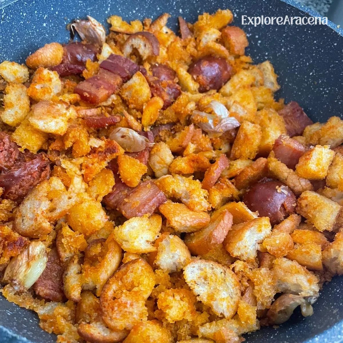 Migas fried breadcrumbs with chorizo, pancetta and whole garlic cloves in a pan at Mesón El Postigo