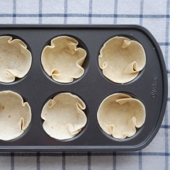 Cắt bánh Tortilla thành những miếng tròn có đường kính vừa với khay cupcake nhà bạn. Ấn các vỏ bánh vào khay cupcake, sau đó múc hỗn hợp bánh gạo sốt cà chua vào gần đầy khuôn. Ở trên rải thêm ít bắp hột, phô thai thái nhỏ. Cho khay cupcake vào lò nướng khoảng 10-15 phút ở 180 độ C là được.