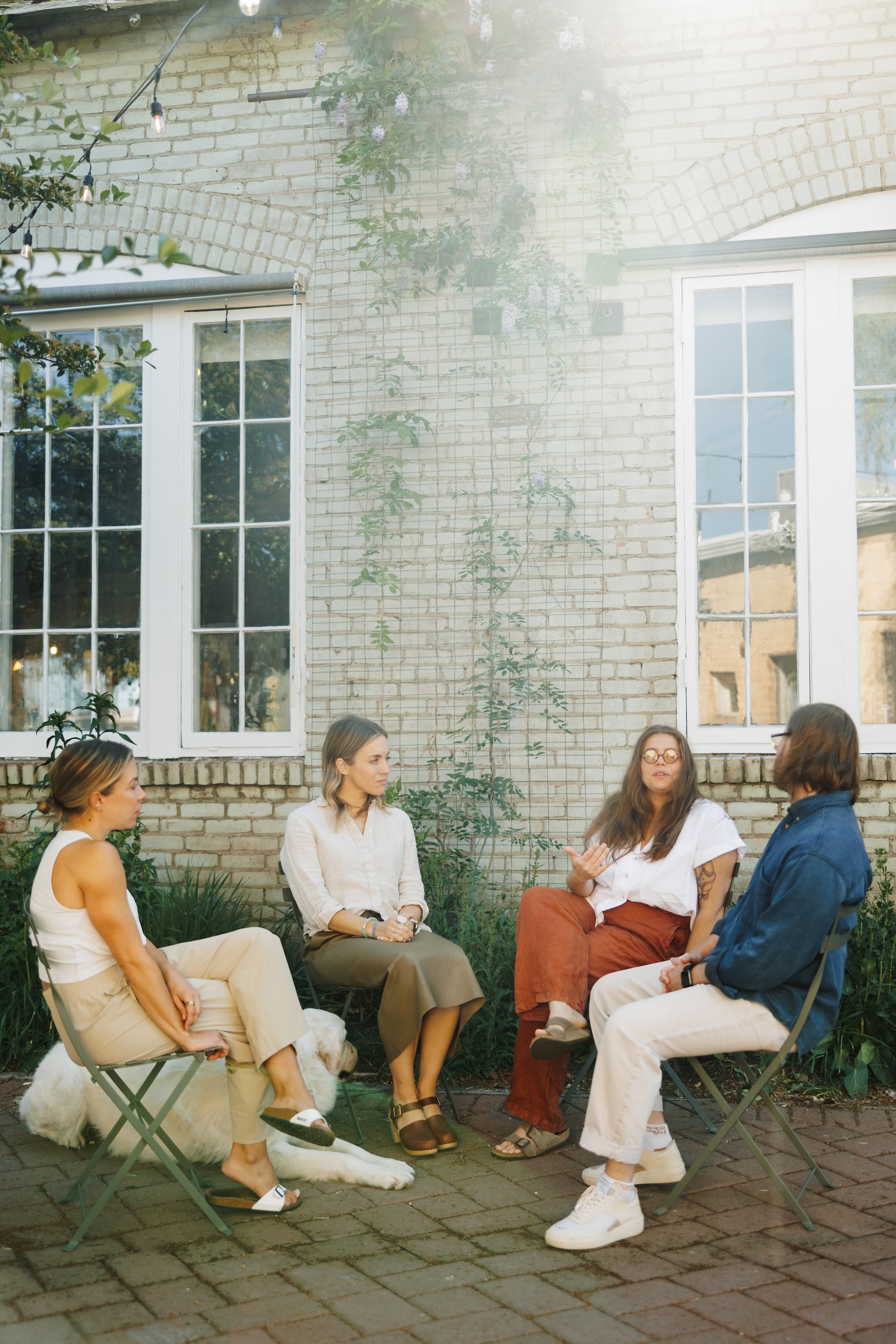 A small group gathered in a sunlit garden outside a white brick house