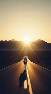 Solitary Figure Walking Towards Sunset on Endless Desert Road