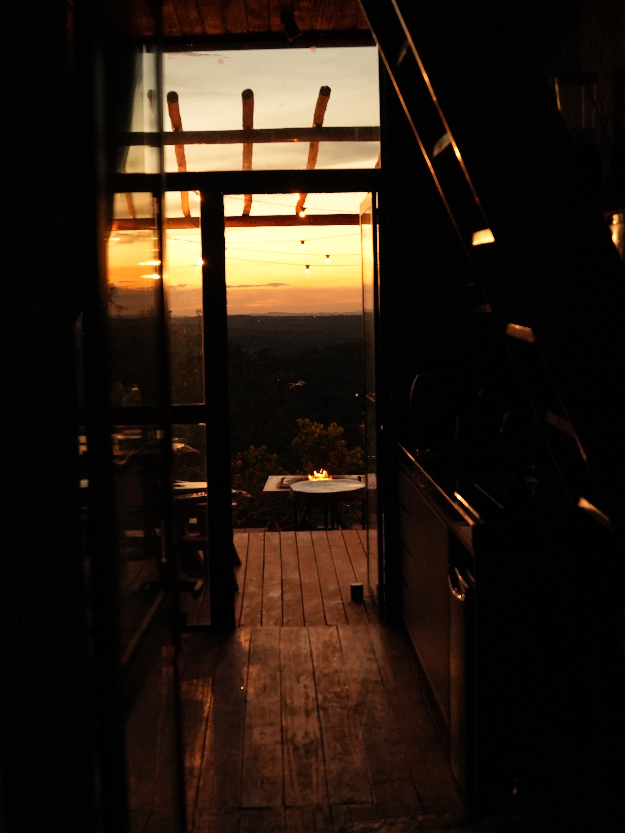 Foto real da vista de dentro do chalé Mei do Mato, olhando pela porta aberta para o deck ao entardecer