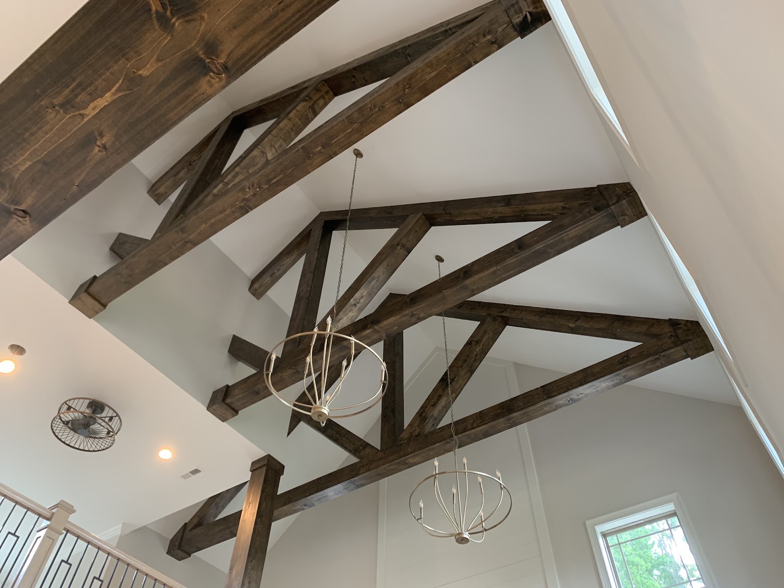 Interior view looking up at a vaulted ceiling with dark wood decorative trusses and hanging metal chandeliers.