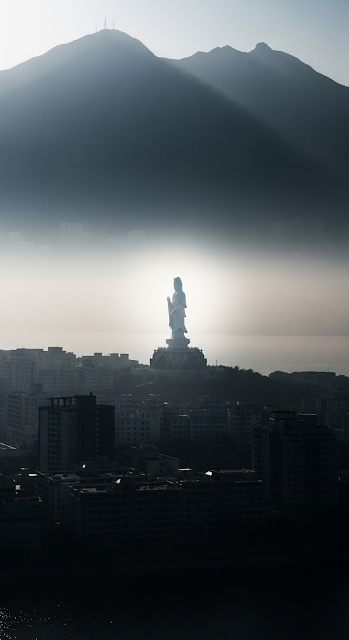 Ethereal View of a White Guanyin Statue Floating Above a Silhouetted Cityscape and Misty Mountains - Free mobile Wallpaper