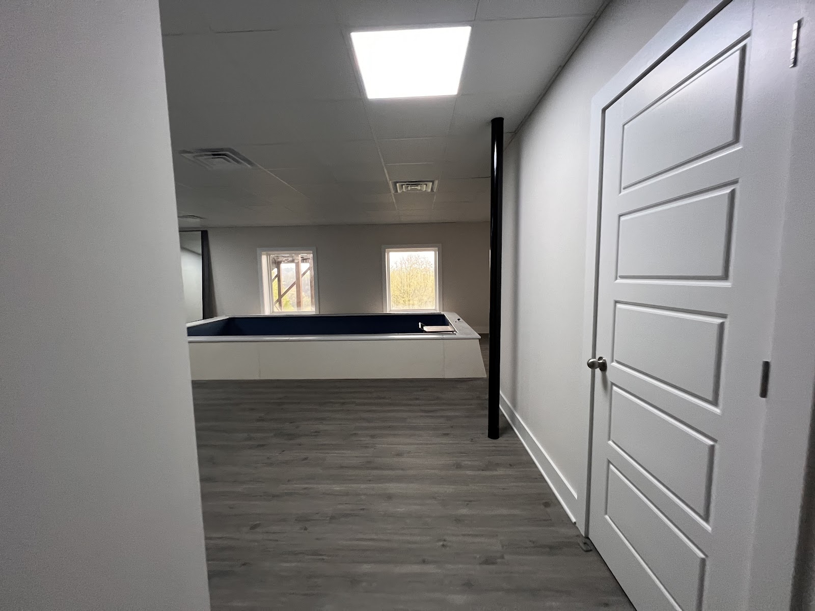Finished interior room in the Inspiration Retreat project with grey flooring, white walls, and a white paneled door.