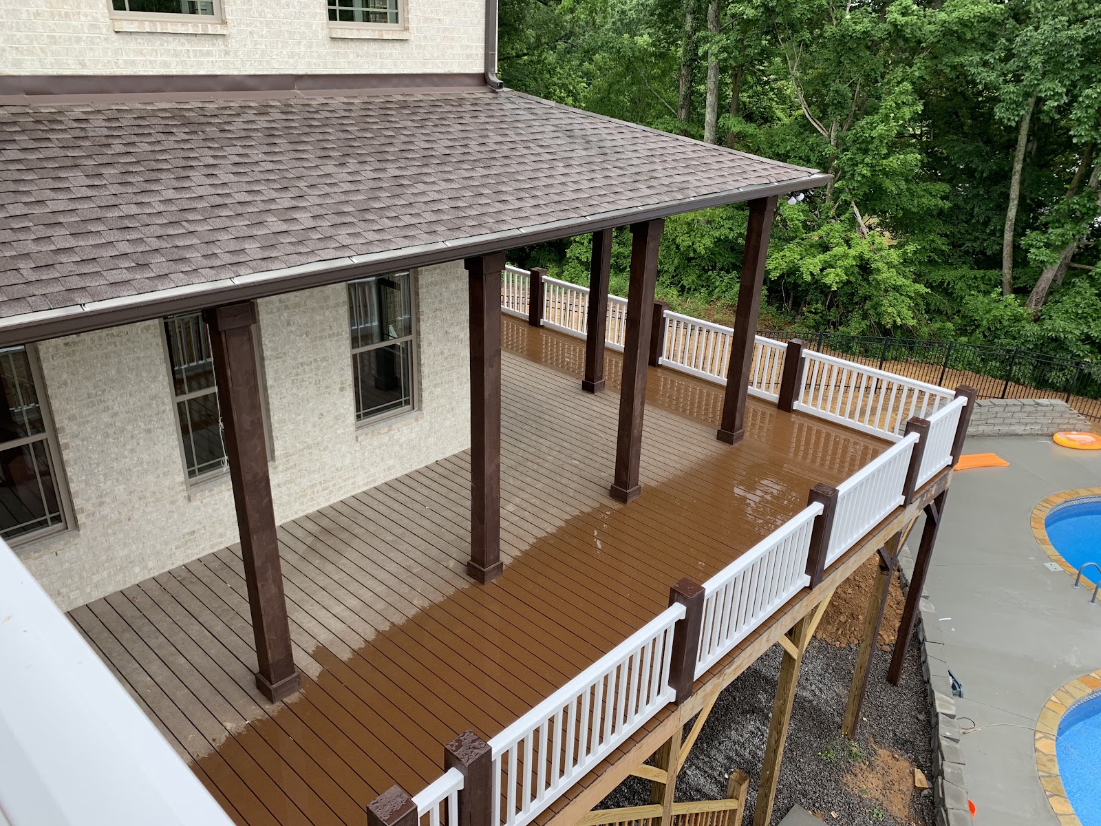 High-angle view of a multi-level wooden deck with white railings and dark support posts, situated next to a swimming pool.