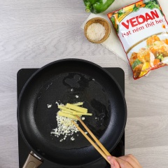 Bắc chảo lên bếp, dầu nóng cho 10gr tỏi băm và 10gr gừng băm vào phi vàng. Vặn lửa lớn, tiếp tục thêm gân bò, củ sen, cà rốt và ớt chuông vào, đảo đều 2 phút.