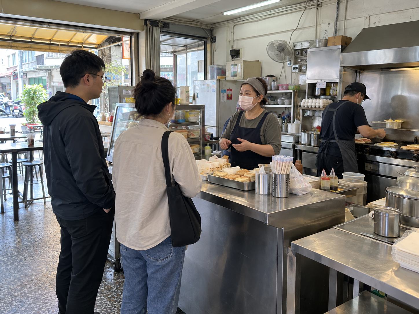 早餐店櫃檯人員向顧客說明等待情況，另一人繼續製作