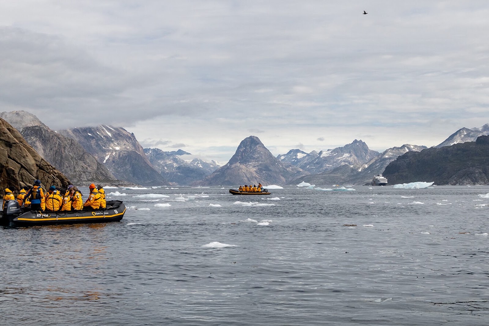 Travelers riding in a Zodiac among icy Arctic waters and dramatic Greenland scenery during an expedition cruise.