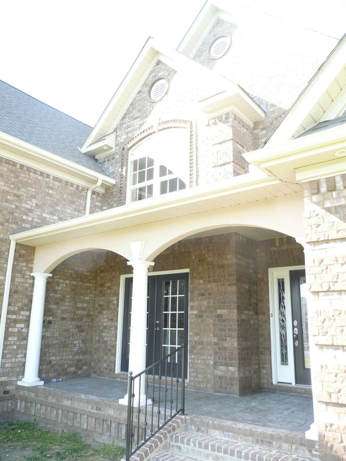 Close-up of a front porch with white columns, arched openings, a brick exterior, and a dark front door with sidelights.