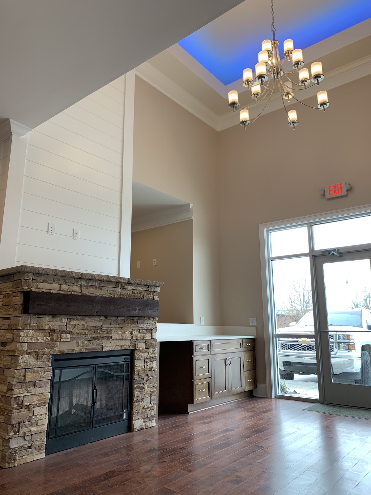 Lobby of a health clinic featuring a stacked stone fireplace, built-in cabinetry, hardwood floors, and a chandelier under a blue-lit tray ceiling.