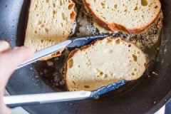 Bắc chảo lên bếp, cho khoảng 1 muỗng canh bơ vào đun nóng, láng bơ khắp mặt chảo. Nhanh tay nhúng bánh mì vào hỗn hợp trứng sữa rồi thả vào chiên vàng 2-3 phút mỗi mặt bánh mì. Bánh mì chiên xong, bạn vớt ra rây để ráo bơ. Lặp lại cho đến khi hết bơ và bánh mì.