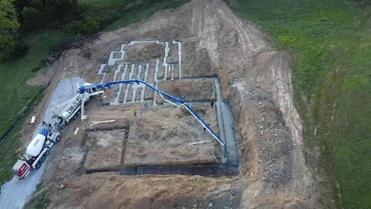 Aerial view of foundation construction for the Brookland project in West Tennessee, featuring a concrete pump truck and mixer pouring concrete into trenches.