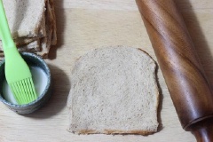 Cắt bỏ mép bánh mì rồi dùng thanh cán cán mỏng tấm bánh. Hòa tan bột bắp với một ít nước, dùng cọ quét hỗn hợp bột ngô xung quanh mép lát bánh mì. Cho phần nhân phô mai vào giữa lát bánh và cuộn lại, dính kín các mép lại.