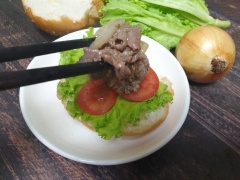 Cắt đôi bánh burger, cho xà lách, cà chua cắt lát lên trên, rồi xếp lên mặt thịt bò xào hành nóng hổi.