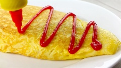 Cho cơm cuộn trứng - omurice ra đĩa (lật mặt trứng chiên tiếp xúc với chảo lên trên), giấu mép trứng xuống đáy đĩa. Cơm chiên bọc trứng thường được ăn cùng tương cà để tạo thêm hương vị và tăng cảm giác ngon miệng.
