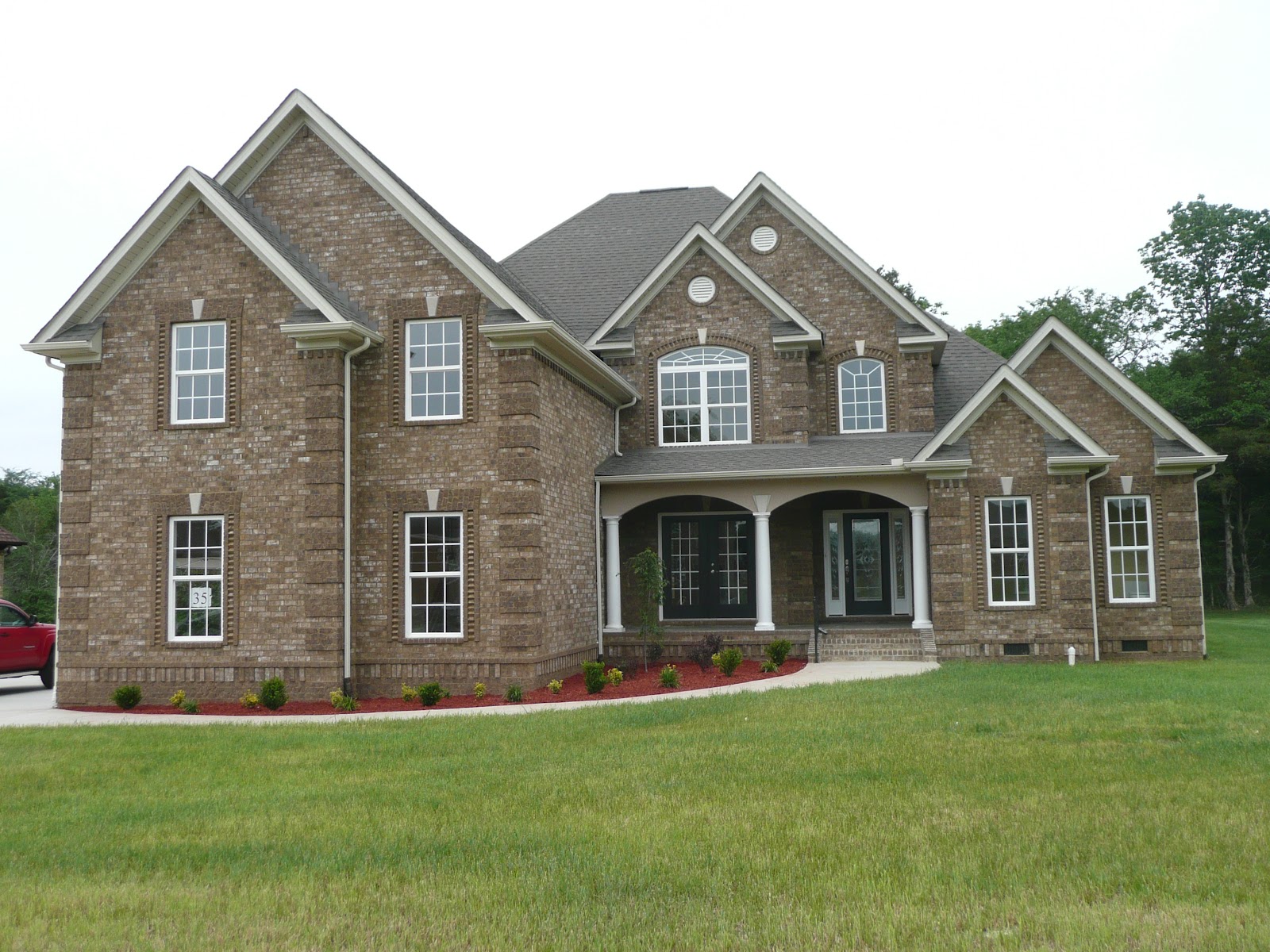 Exterior view of a large two-story brick house with multiple gables, white-trimmed windows, and a front porch with columns.