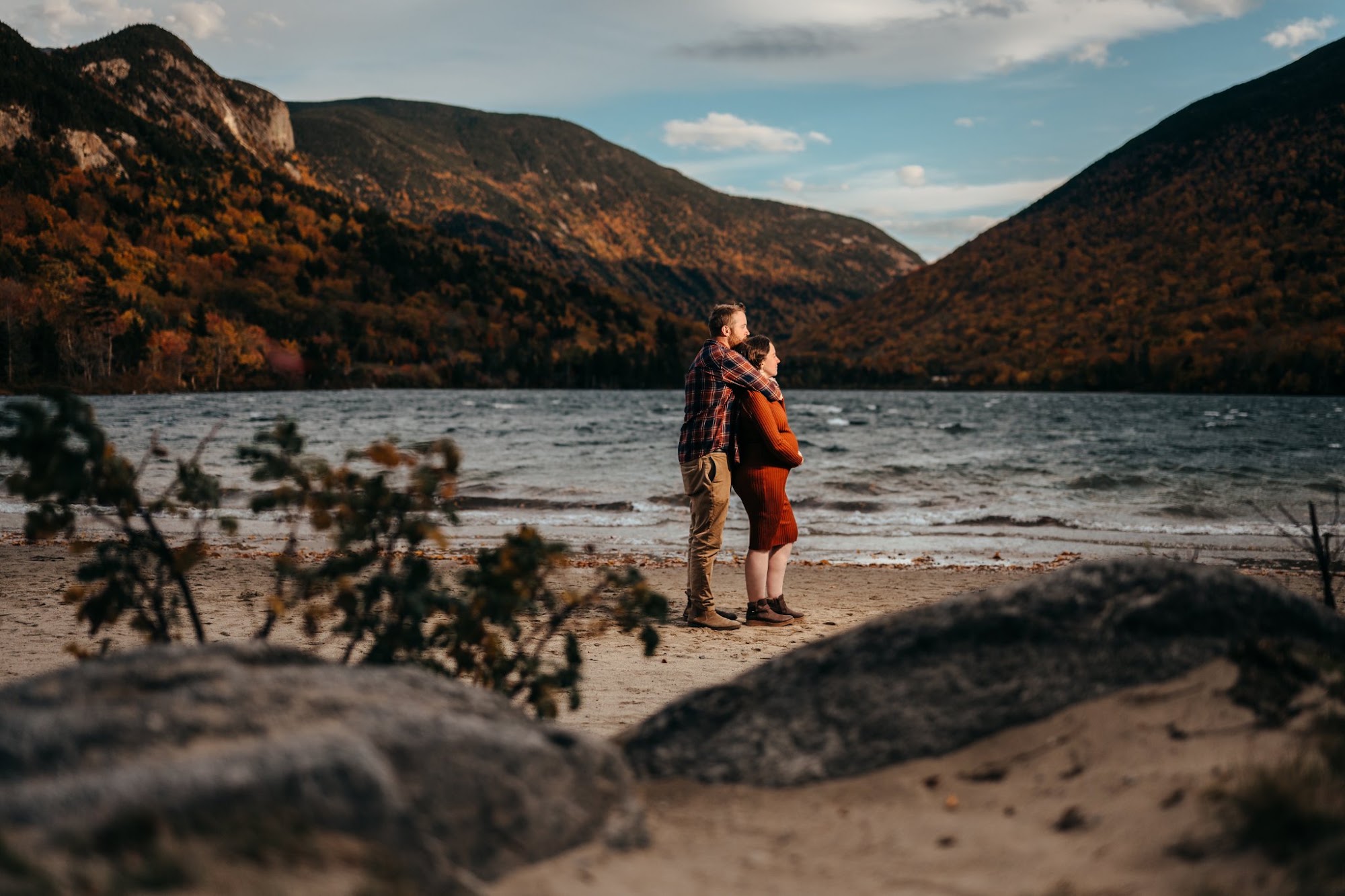 Zack and Holly on the wide beach with rocks in the foreground, looking out over the lake