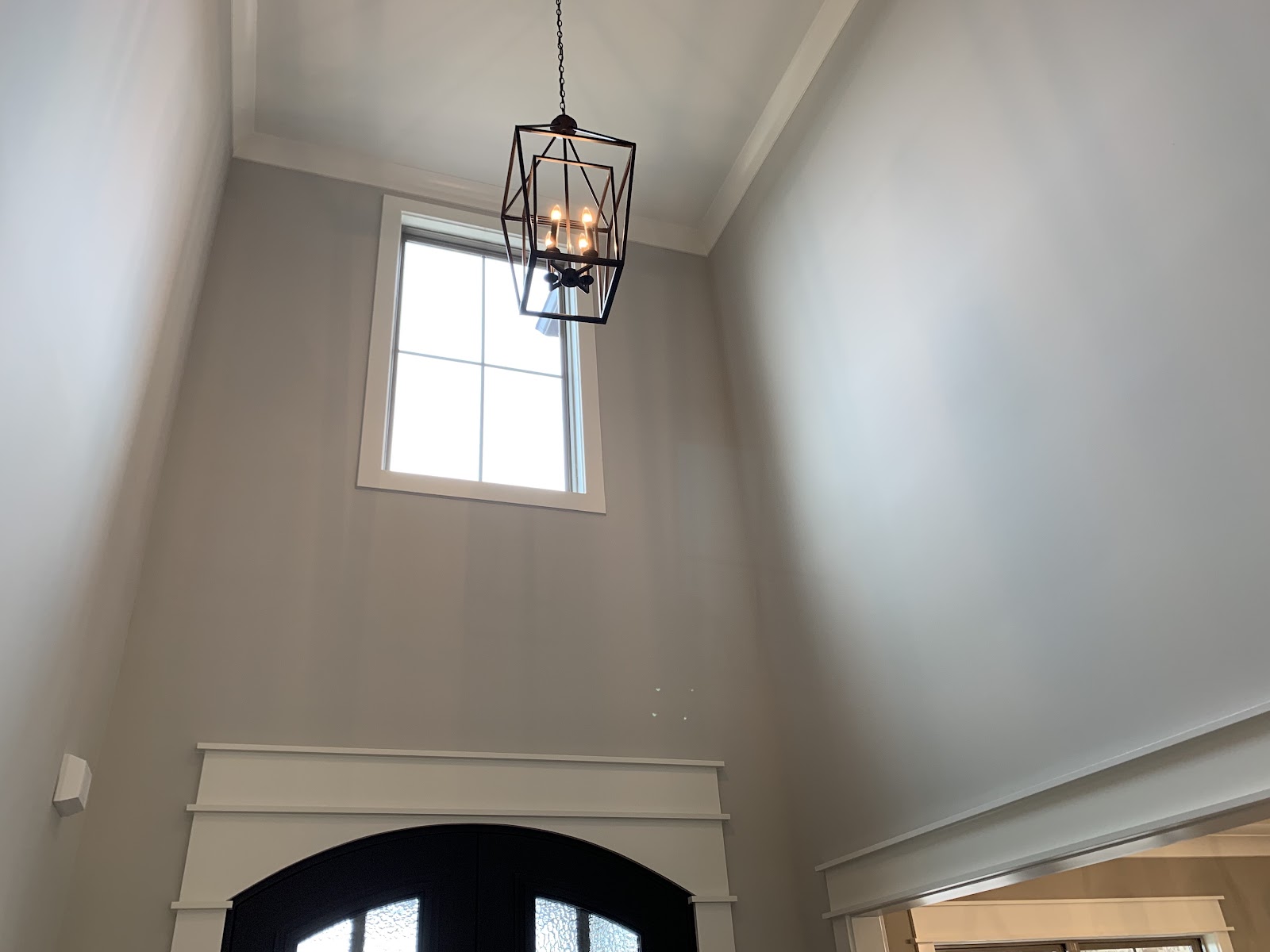 High-ceiling entryway featuring a black lantern-style pendant light, a high-set window, and the top of dark arched double doors.