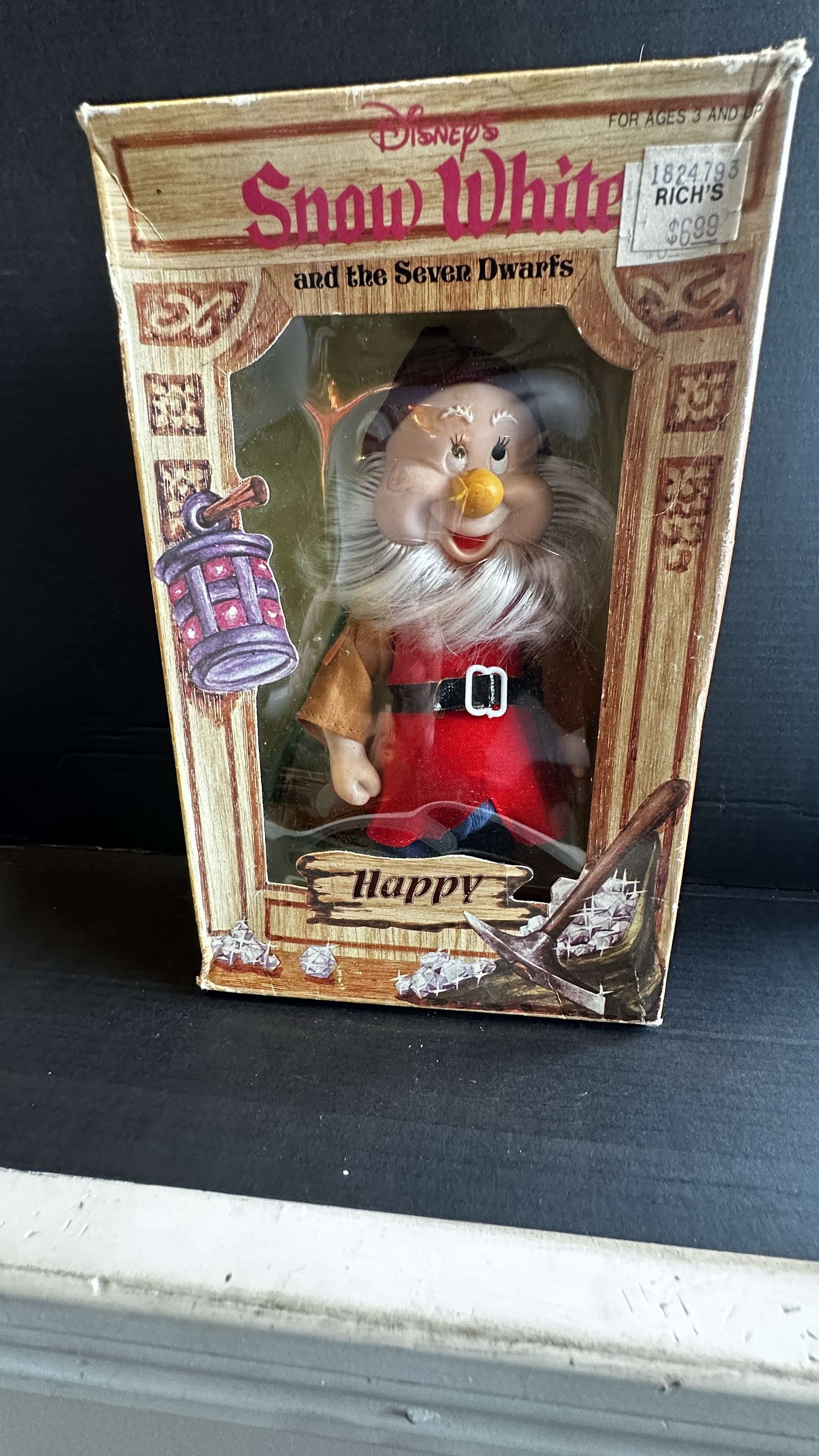 Boxed Happy dwarf soft-body doll from Walt Disney Productions, late 1970s to early 1980s, in original window box with pickaxe and gem graphics and a Rich's department store price tag