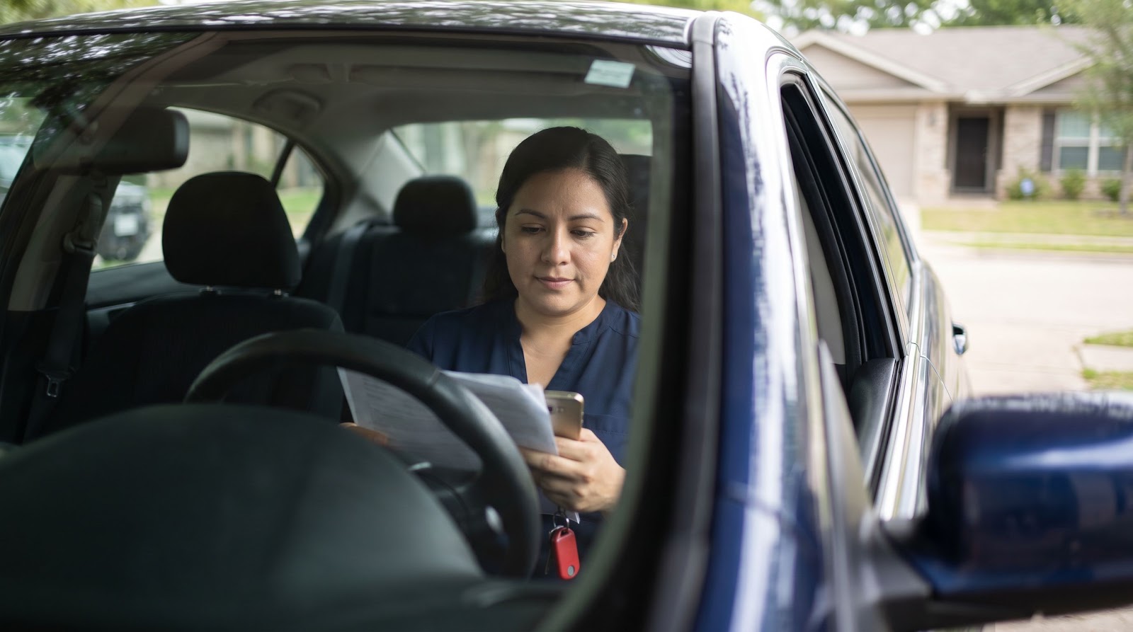 Hispanic Texas commuter reviewing texas rush hour car accident insurance coverage inside her car before driving to work