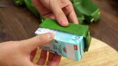 Để gấp chiếc thuyền bằng lá chuối, bạn chuẩn bị dụng cụ gồm 1 hộp sữa cỡ vừa và khoảng 100gr lá chuối. Cắt lá chuối sao cho khi gấp lên chiều ngang ôm vừa thân hộp sữa, chiều dài gấp đôi hộp sữa. Để không bị giòn rách khi gấp, bạn trụng sơ lá chuối với nước sôi cho lá được mềm hơn, sau đó để ráo. Gấp hai mép lại rồi cố định bằng tăm, cắt phần thừa của đầu tăm rồi lấy hộp sữa ra, vậy là bạn đã có chiếc thuyền lá chuối thật xinh rồi.