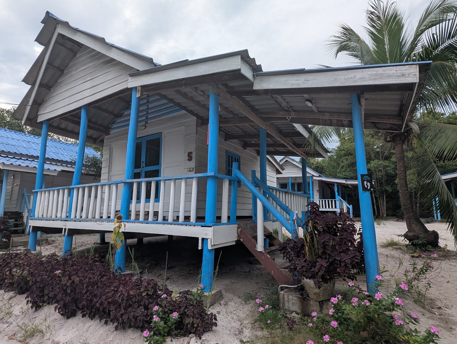 A single room bungalow lifted on blue stilts/columns that
                 rise to the roof in among a white painted railing to match the
                 white painted walls