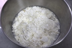 Rây 1kg bột mì và 10g men nở (lượng men = 1-2% lượng bột) vào thố nhồi bột, đổ 600ml nước lạnh vào (nếu mùa đông thì bạn dùng nước ấm nhé - lượng nước là 55-60% lượng bột). Bật máy trộn và nhồi bột thành khối đồng nhất. Sau đó bọc màng thực phẩm để nhiệt độ phòng cho bột bánh bao nở gấp đôi.