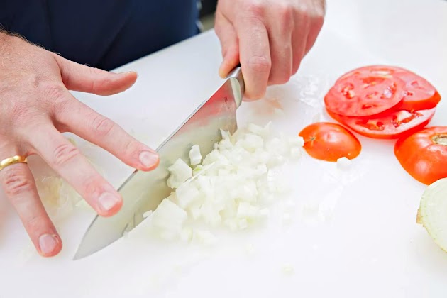 Manos de una persona cortando cebollas en una tabla de cortar con un cuchillo del juego de 8 piezas Ginsu Gourmet Chikara Series