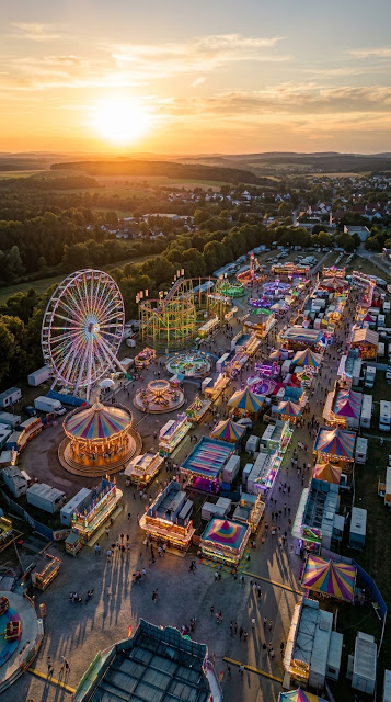 Aerial View of a Colorful Carnival with Ferris Wheel at Sunset - Free mobile Wallpaper