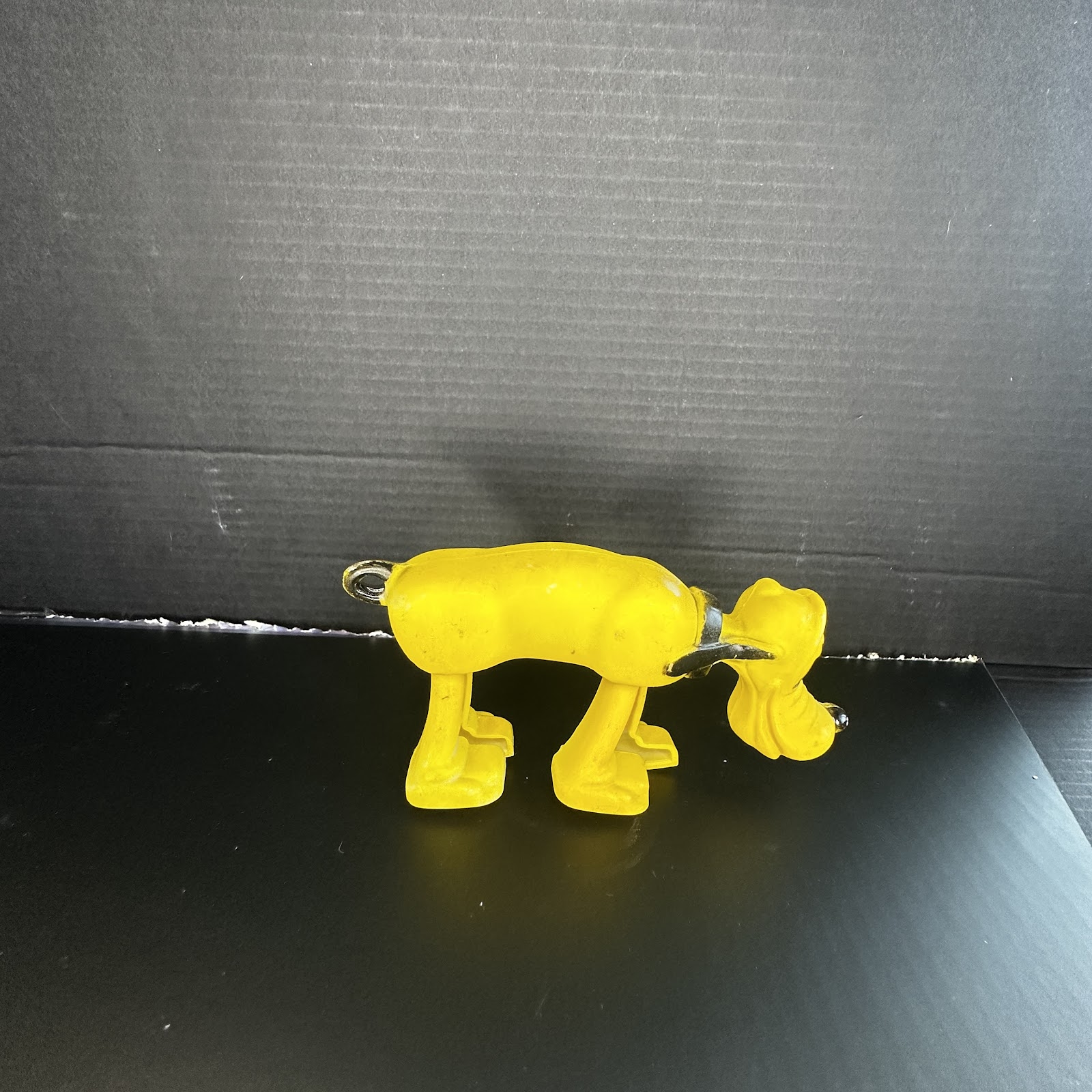 Vintage Sun Rubber Co. molded rubber Pluto squeak toy in sniffing pose, yellow body with black painted details, showing age-appropriate paint wear
