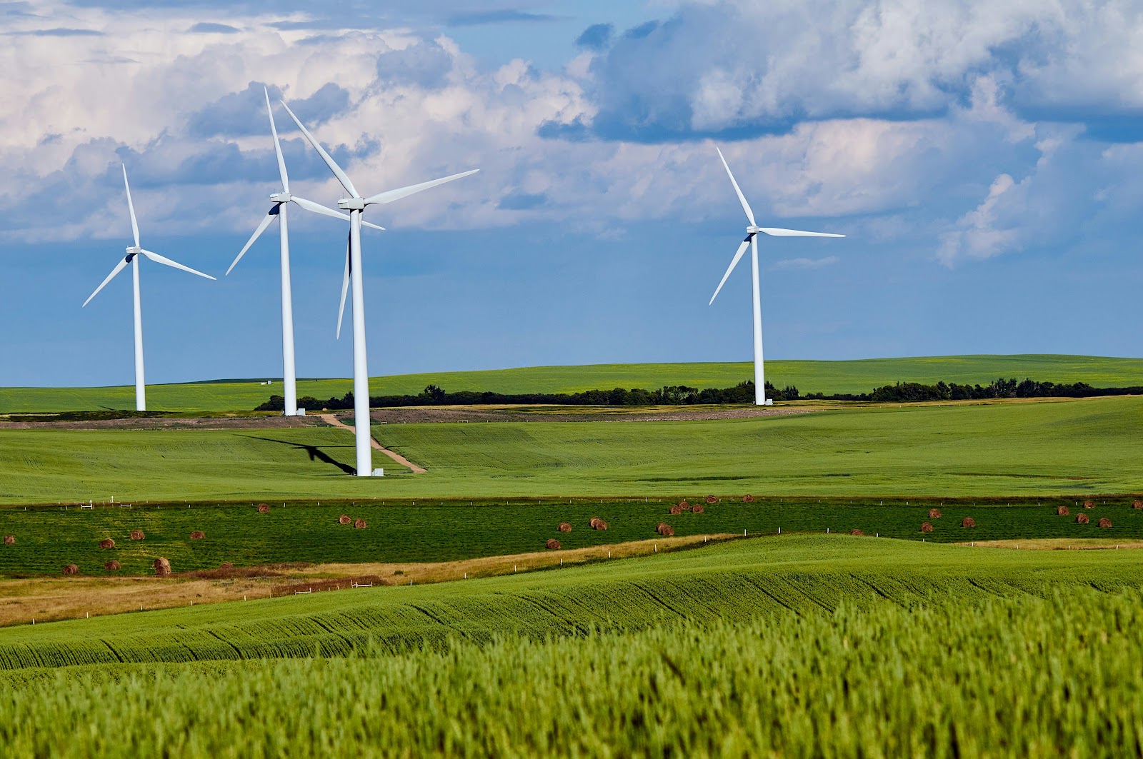 4 Wind Turbines on Green Grass Field on Cloudy Blue Sky Representing Green Inflation