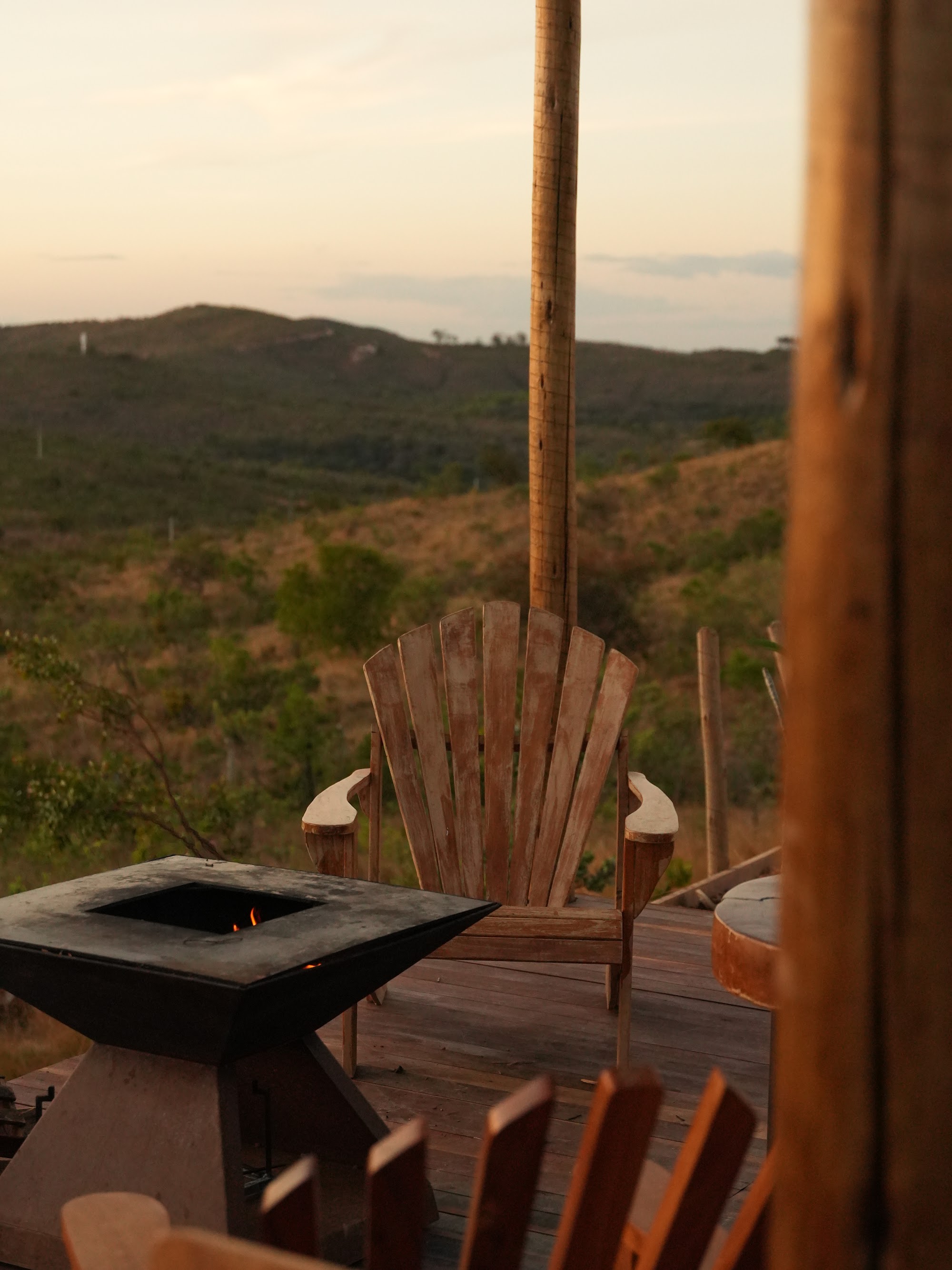 Foto real do deck do chalé Mei do Mato ao entardecer, com cadeira vazia e vista aberta para a Serra do Cipó