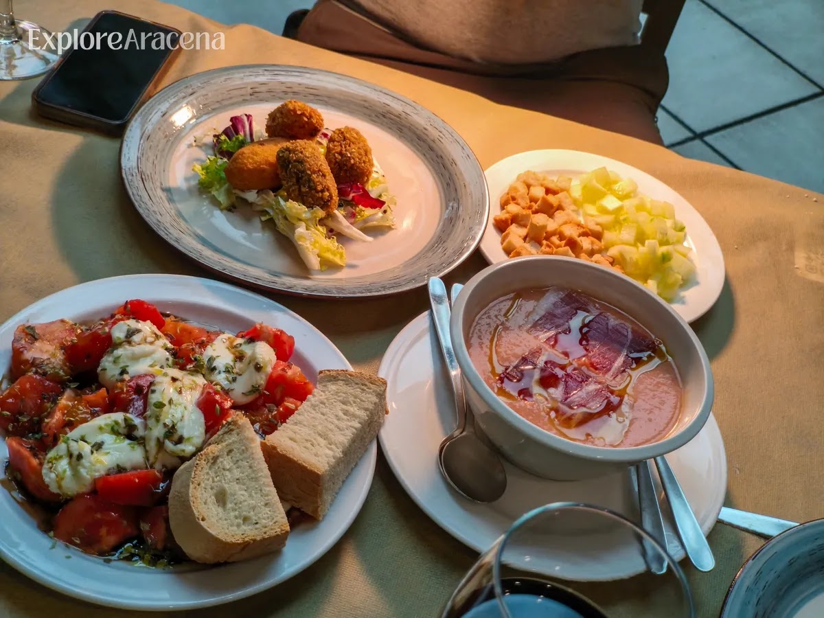 Traditional summer dishes at Restaurante José Vicente in Aracena, including salmorejo, croquetas, and fresh tomato with local cheese.