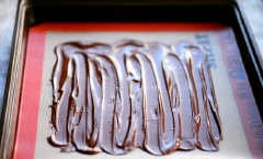 Chocolate đen và trắng bạn chọn loại tùy thích nhé. Nếu không tìm thấy kẹo chocolate dâu tây, bạn có thể chọn bất cứ loại kẹo này có màu đỏ. Về kẹo bạc hà thì nên mua loại kẹo gậy (Candy canes) nhé. Đem chochoclate đen đun cách thủy cho nóng chảy. Phết trước lớp chocolate đen lên giấy nến.