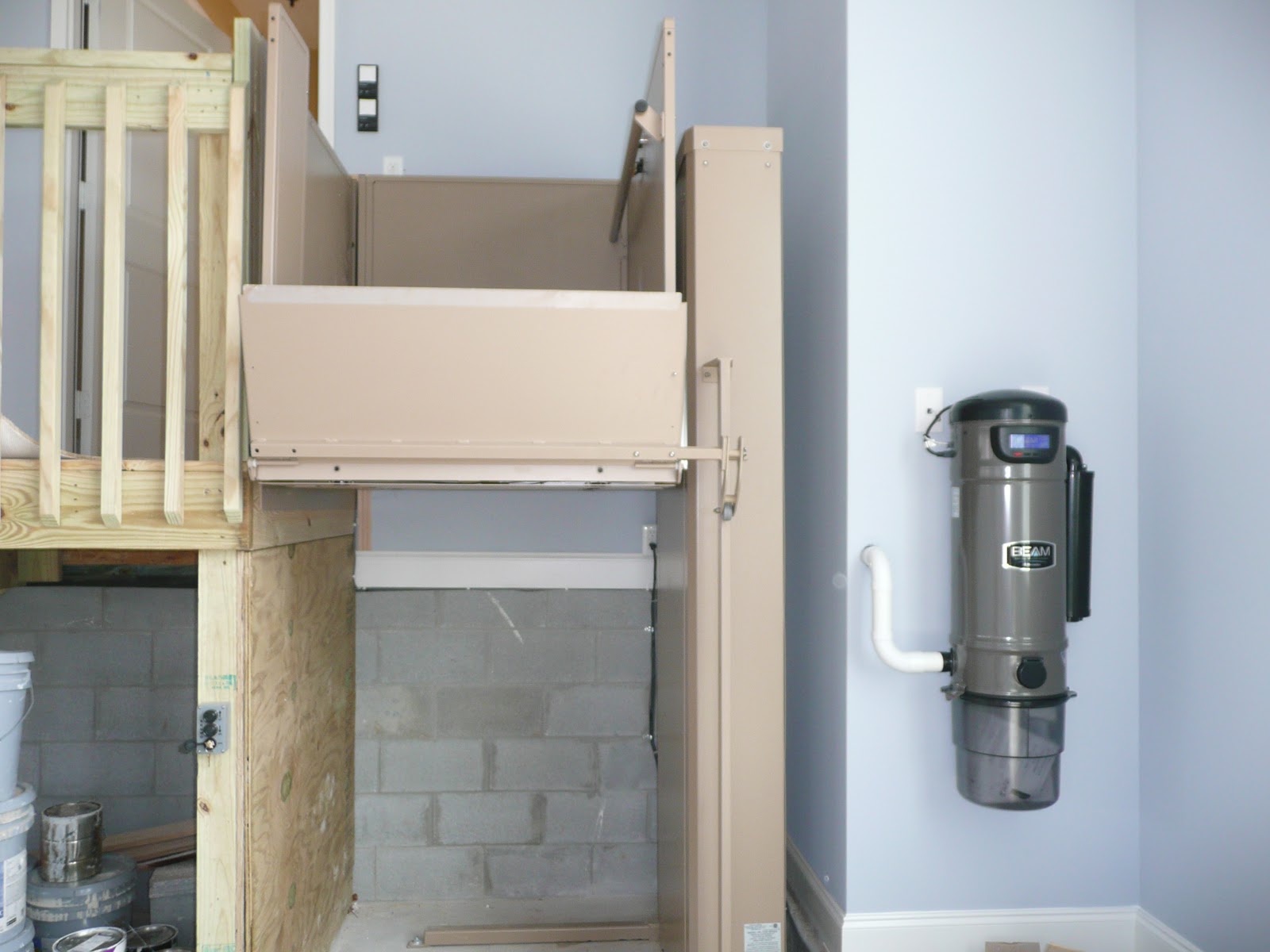 A beige platform lift installed next to a wooden landing with a railing in a room under construction.