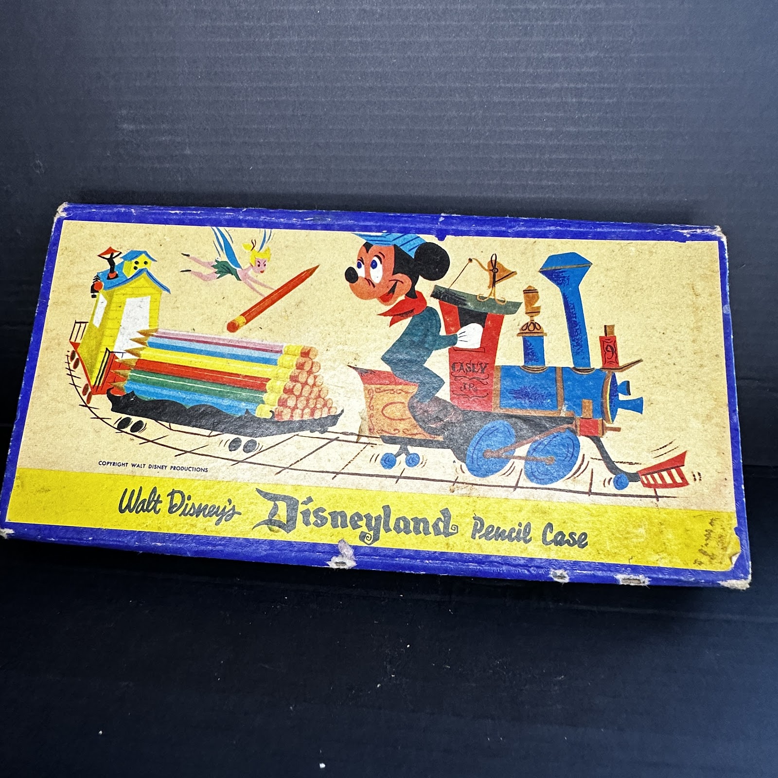 Vintage 1950s Disneyland cardboard pencil case with lithographed paper wrap showing Mickey Mouse in engineer cap on Casey Jr. train and Tinker Bell holding a pencil, with Disneyland gothic logo