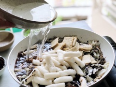 Cho tiếp chả cá, bánh gạo và 300ml nước vào chảo, trộn đều và đun lửa vừa cho đến khi bánh gạo chín mềm vừa miệng và sốt trở nên sệt hơn.