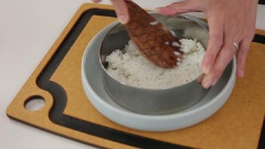 Dùng cọ quết bên trong khuôn bánh bằng một lớp dầu ăn mỏng, sau đó, múc cơm trắng đổ vào trong rồi dùng muỗng dàn đều cơm trong lòng khuôn. Để muỗng không bị dính cơm, bạn có thể nhúng ướt nó trước khi dàn đều.