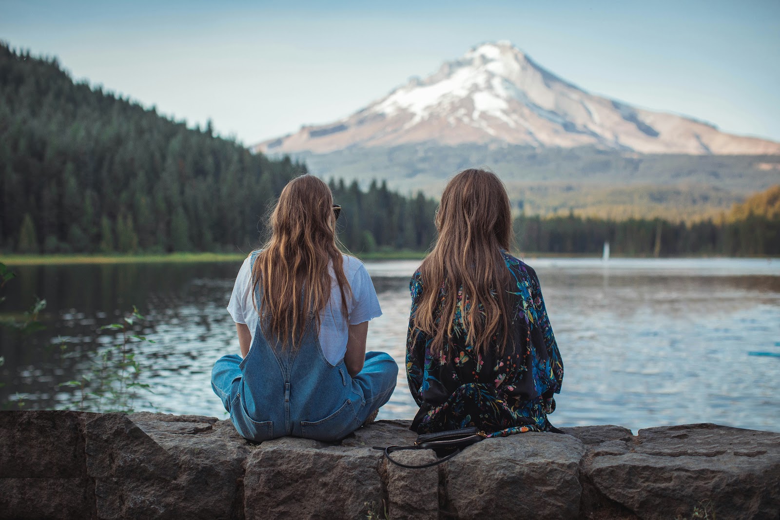 Two people sitting beside Trillium Lake looking toward a snow-capped Mount Hood