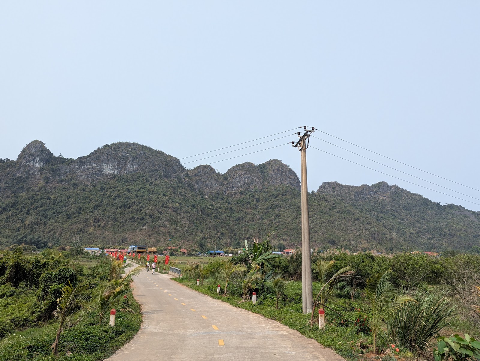 A photo of a concrete path with some telephone cables passing overhead and a
                 lush range of mountains in the background.