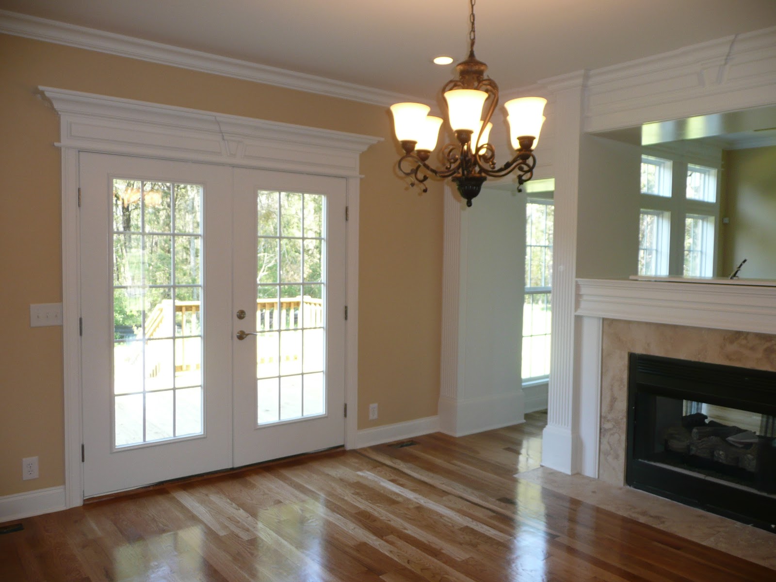 Interior room featuring white French doors with a decorative header, hardwood floors, a chandelier, and a partial view of a fireplace.